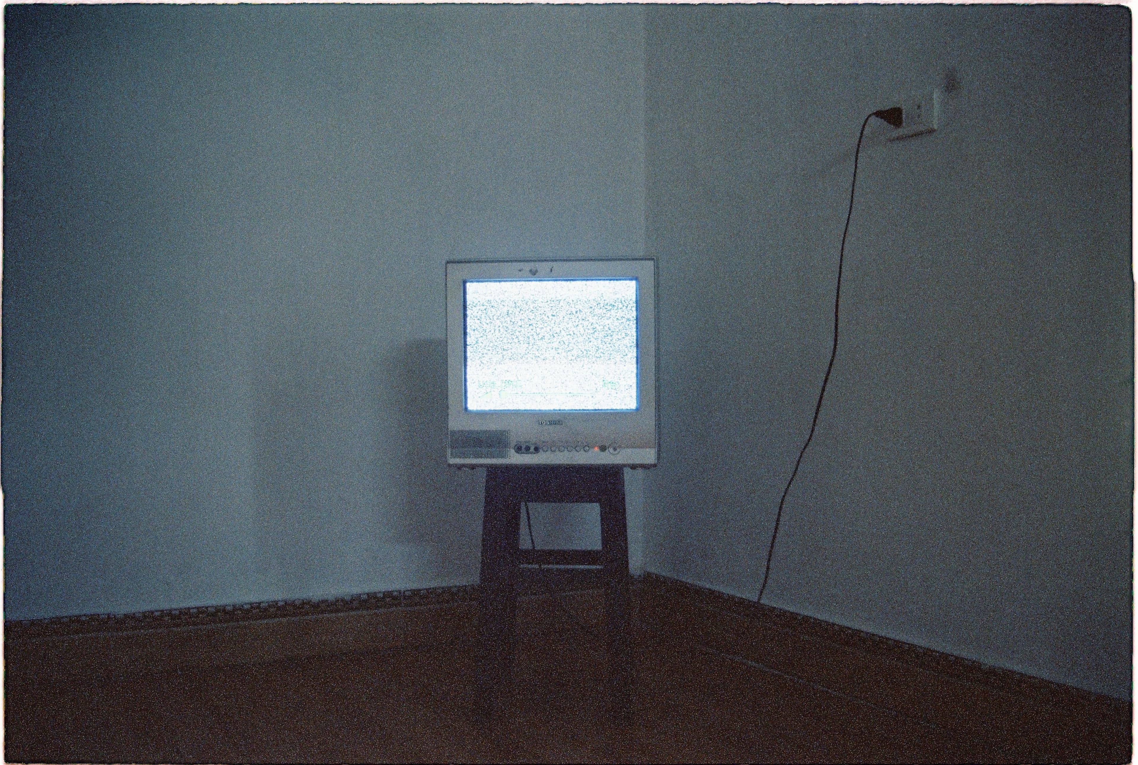 A lone vintage CRT television on a stool against a distressed wall